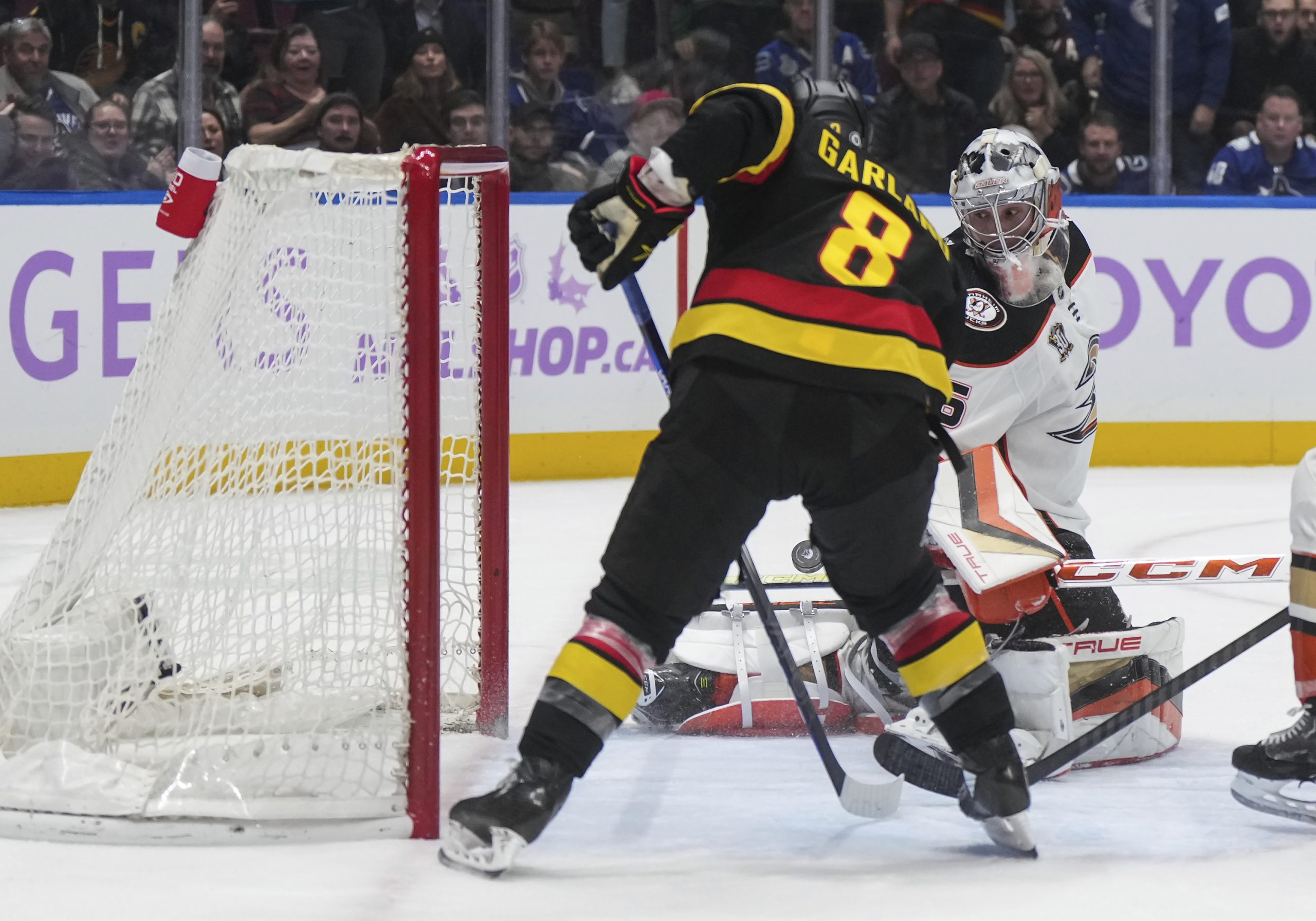 Ducks goalie John Gibson, back right, stops the Vancouver Canucks’...