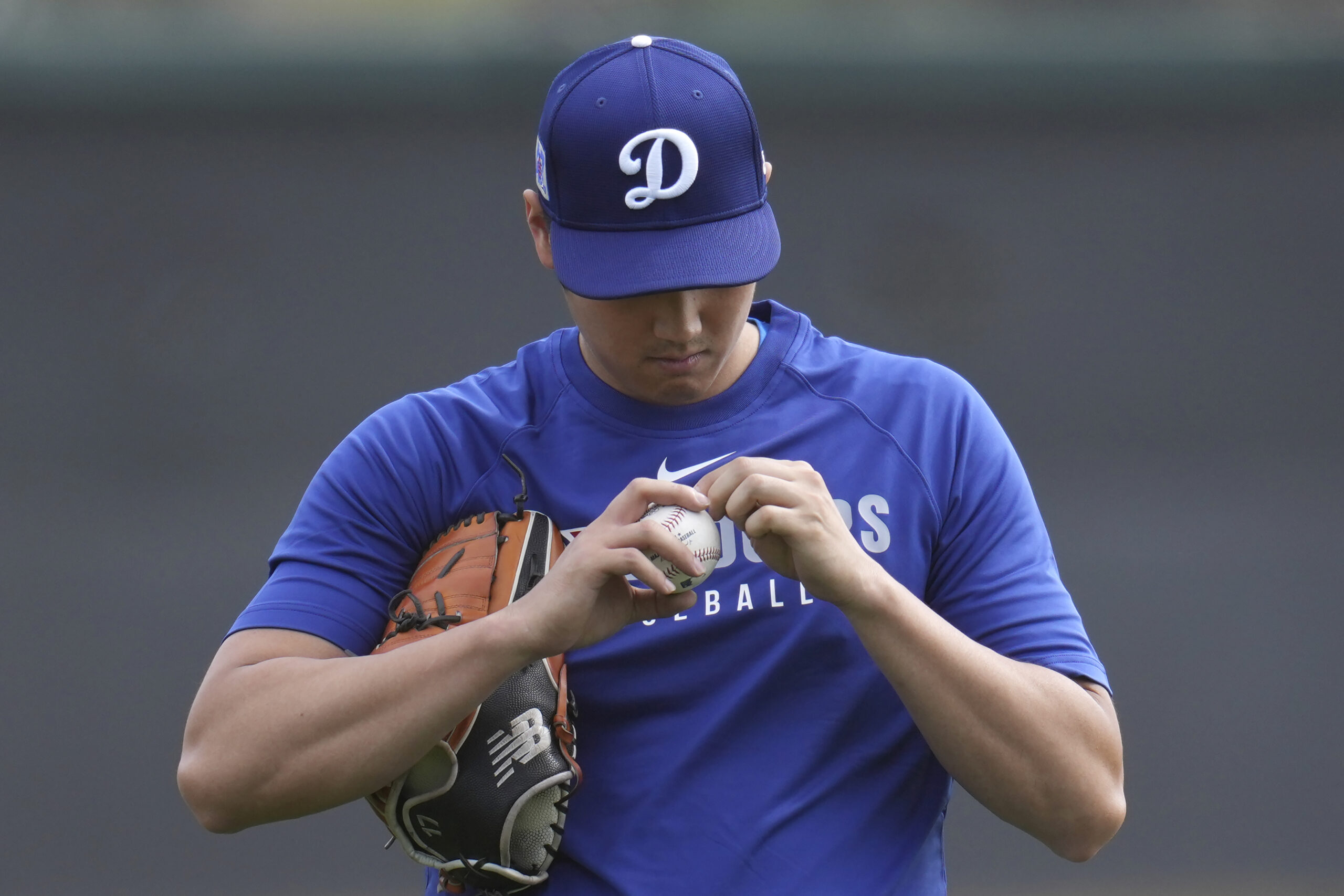 Dodgers star Shohei Ohtani examines the stitching on a baseball...