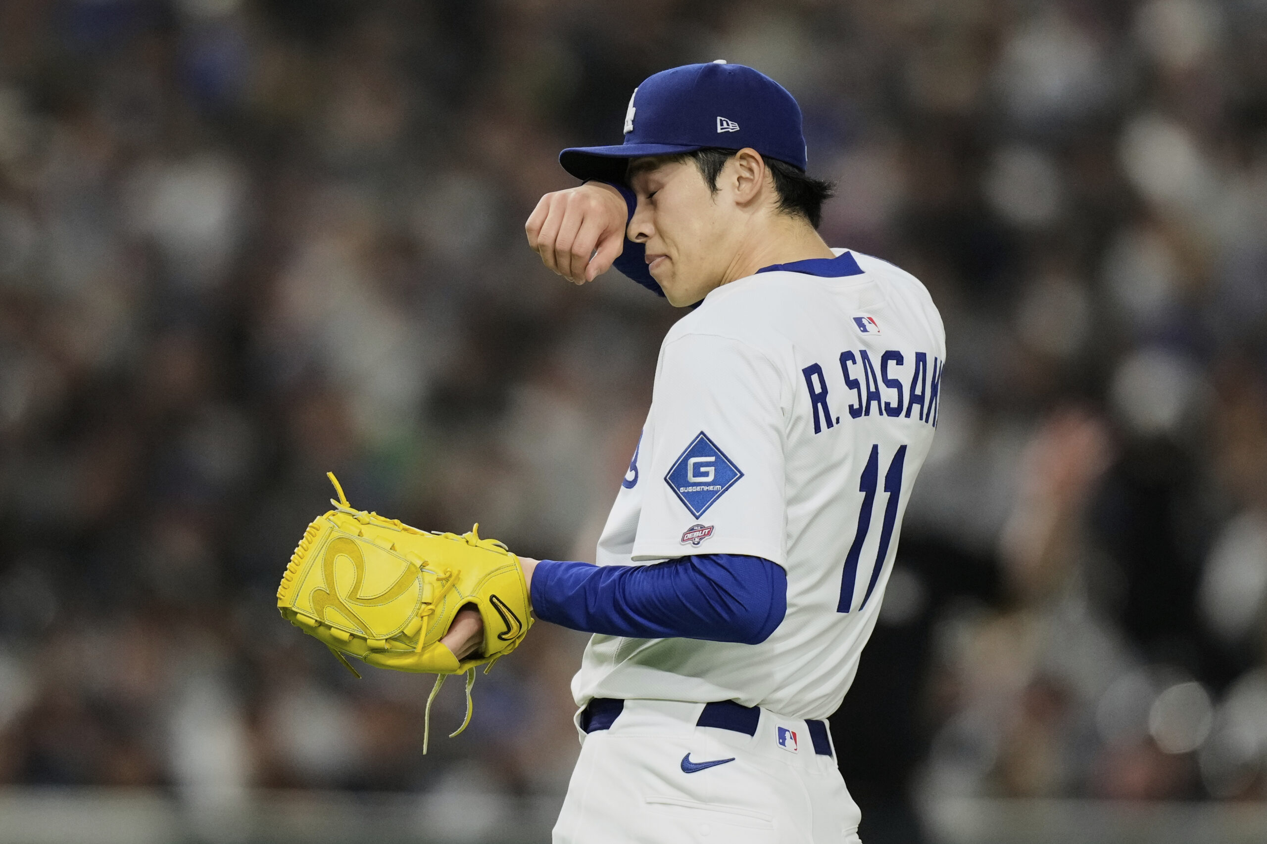 Dodgers pitcher Roki Sasaki wipes his face as he works...