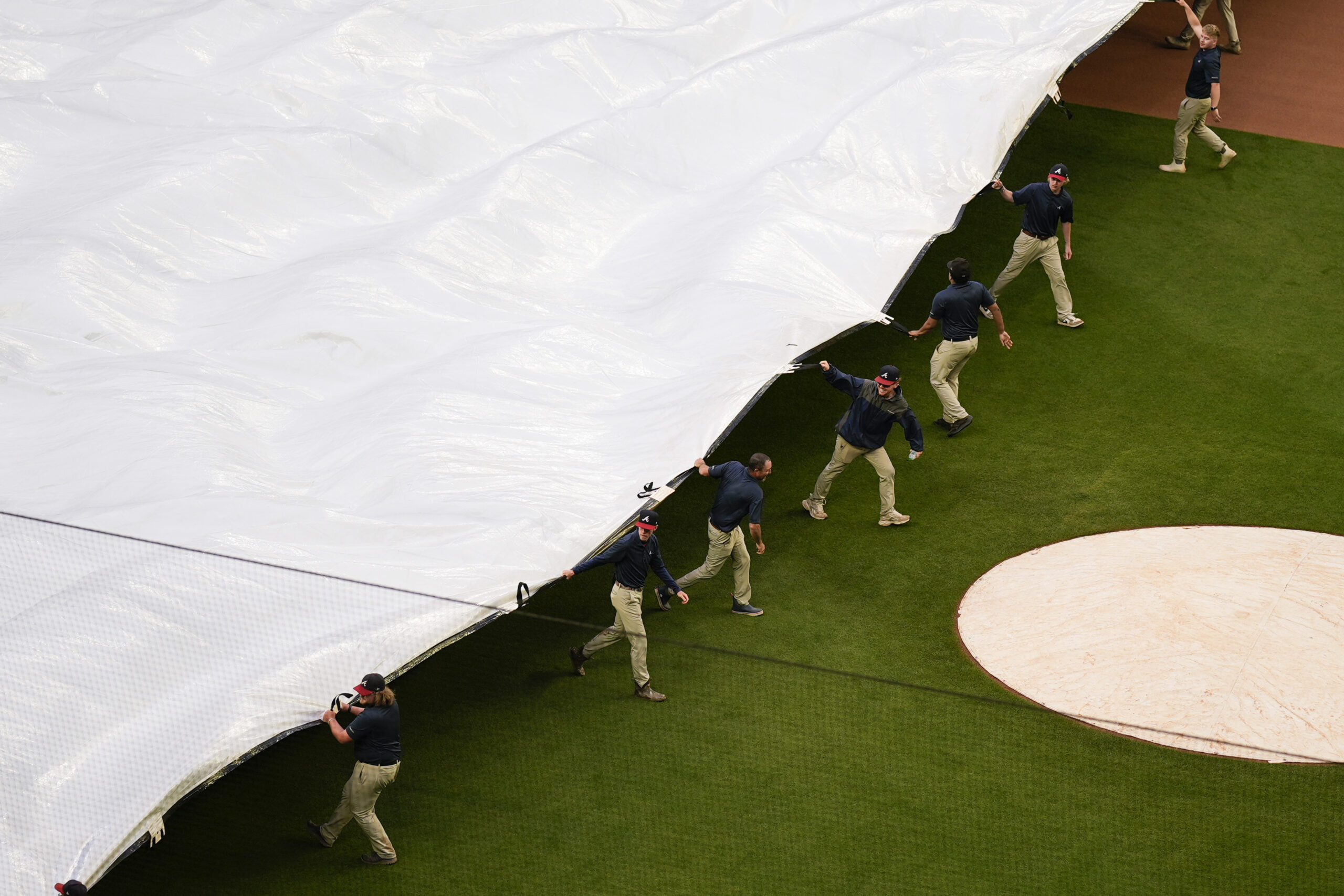 Crews cover the field before a rain-delayed baseball game between...
