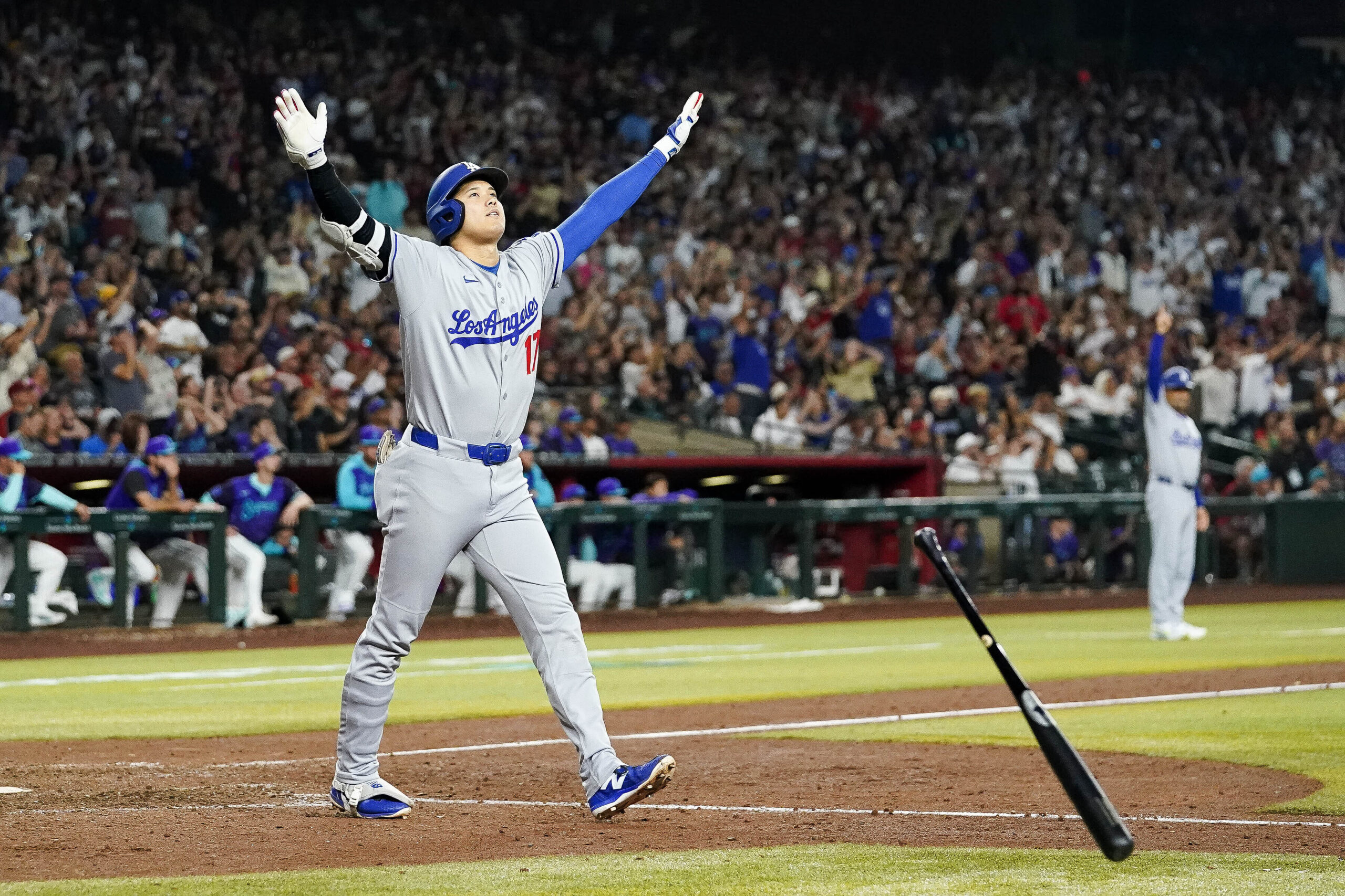 Dodgers star Shohei Ohtani tosses his bat as he begins...