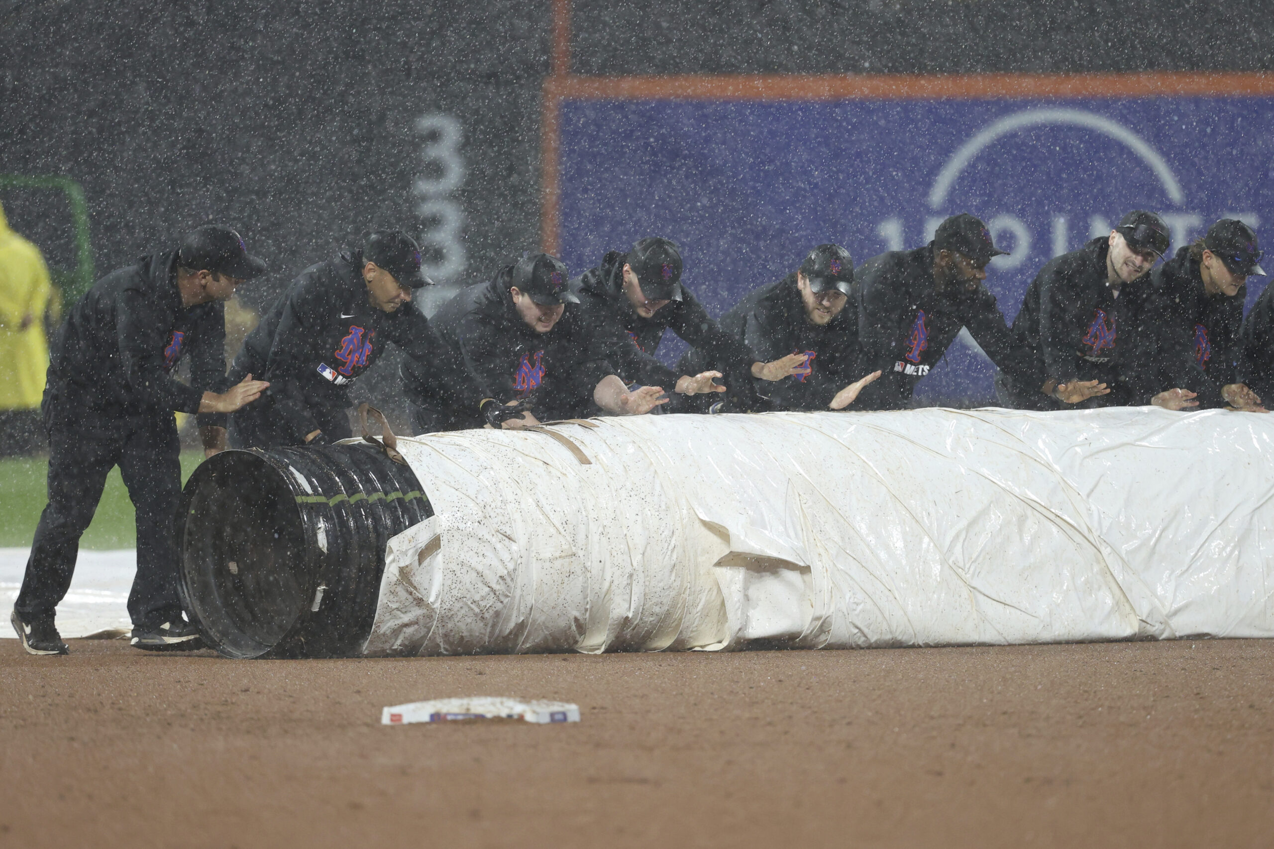 Grounds crew members cover the field as it rains during...