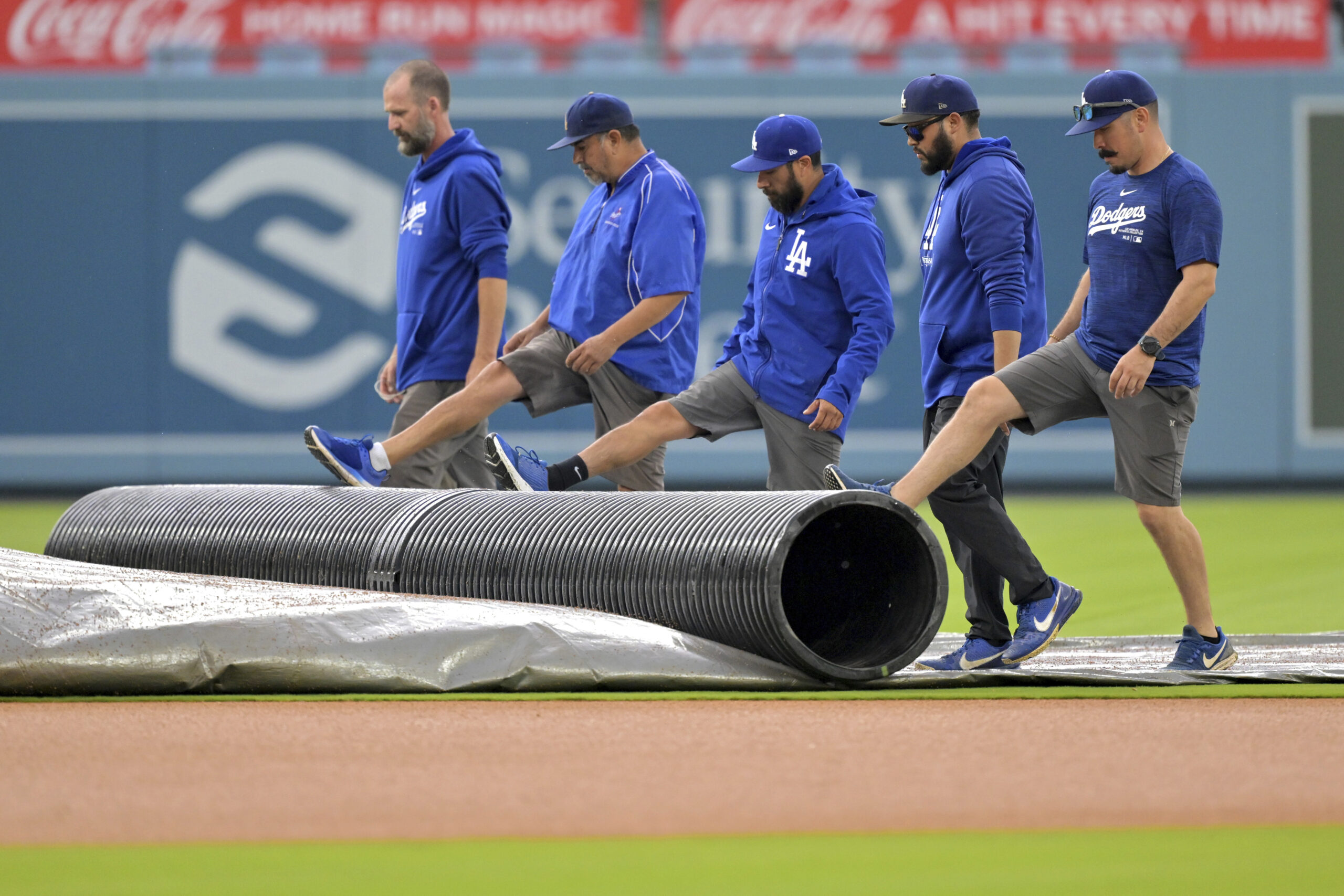 Grounds crew workers roll up a tarp covering the infield...