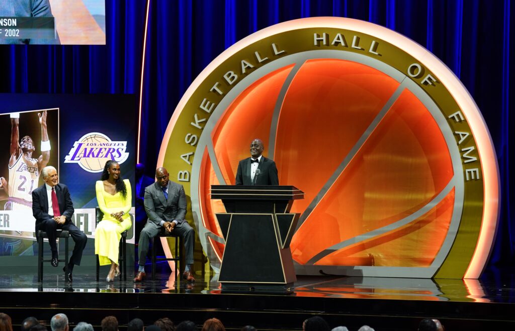 Oct 13, 2024; Uncasville, Conn, USA; Class of 2024 inductee Michael Cooper speaks alongside presenters Magic Johnson (‘02), Pat Riley (‘08) and Lisa Leslie (‘15) during the Naismith Memorial Basketball Hall of Fame Enshrinement at Symphony Hall Springfield. Mandatory Credit: David Butler II-Imagn Images