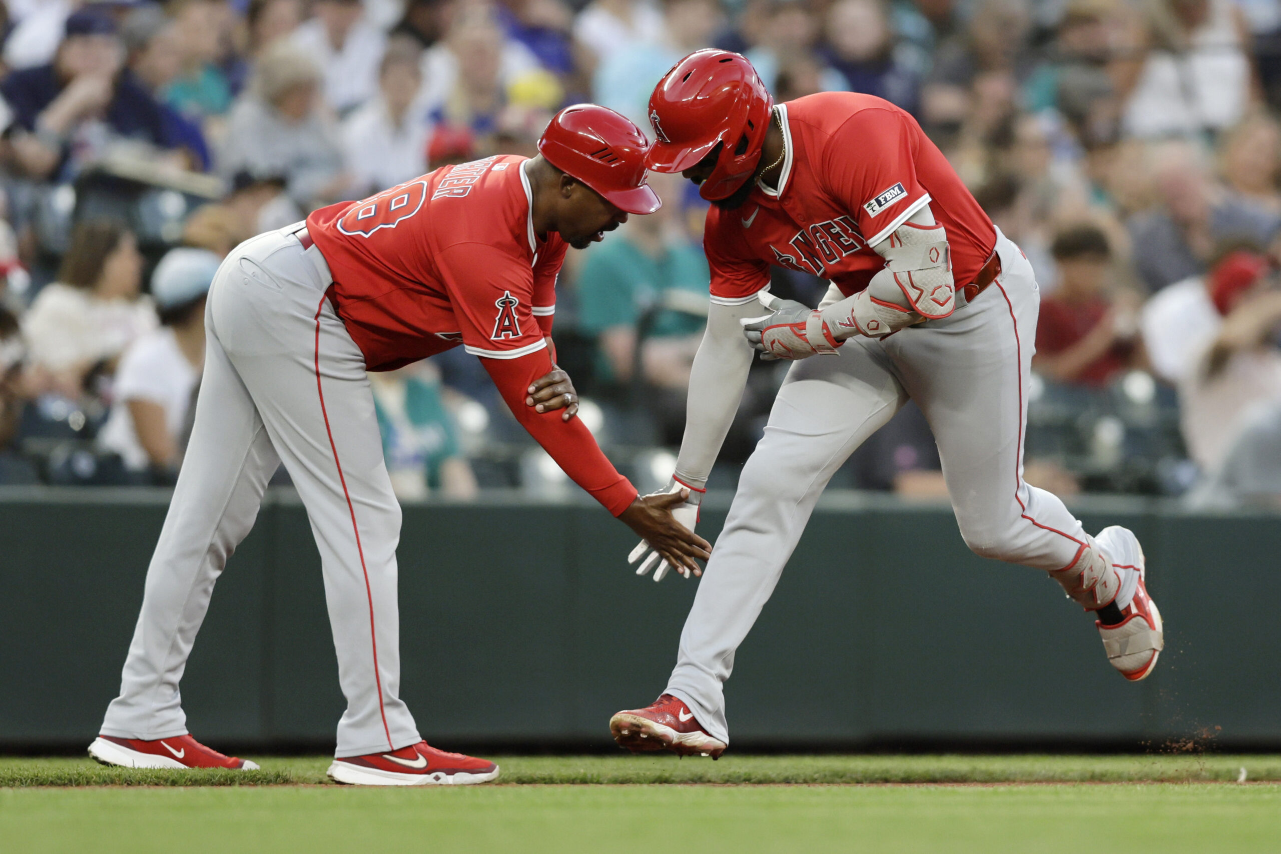 Angels’ Jo Adell, right, is greeted by third base coach...
