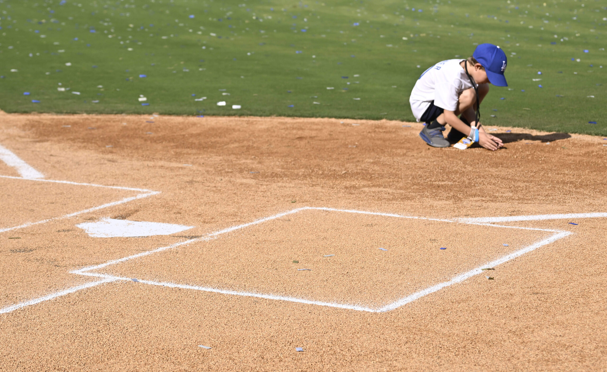 A young boy picks up some dirt at home plate...