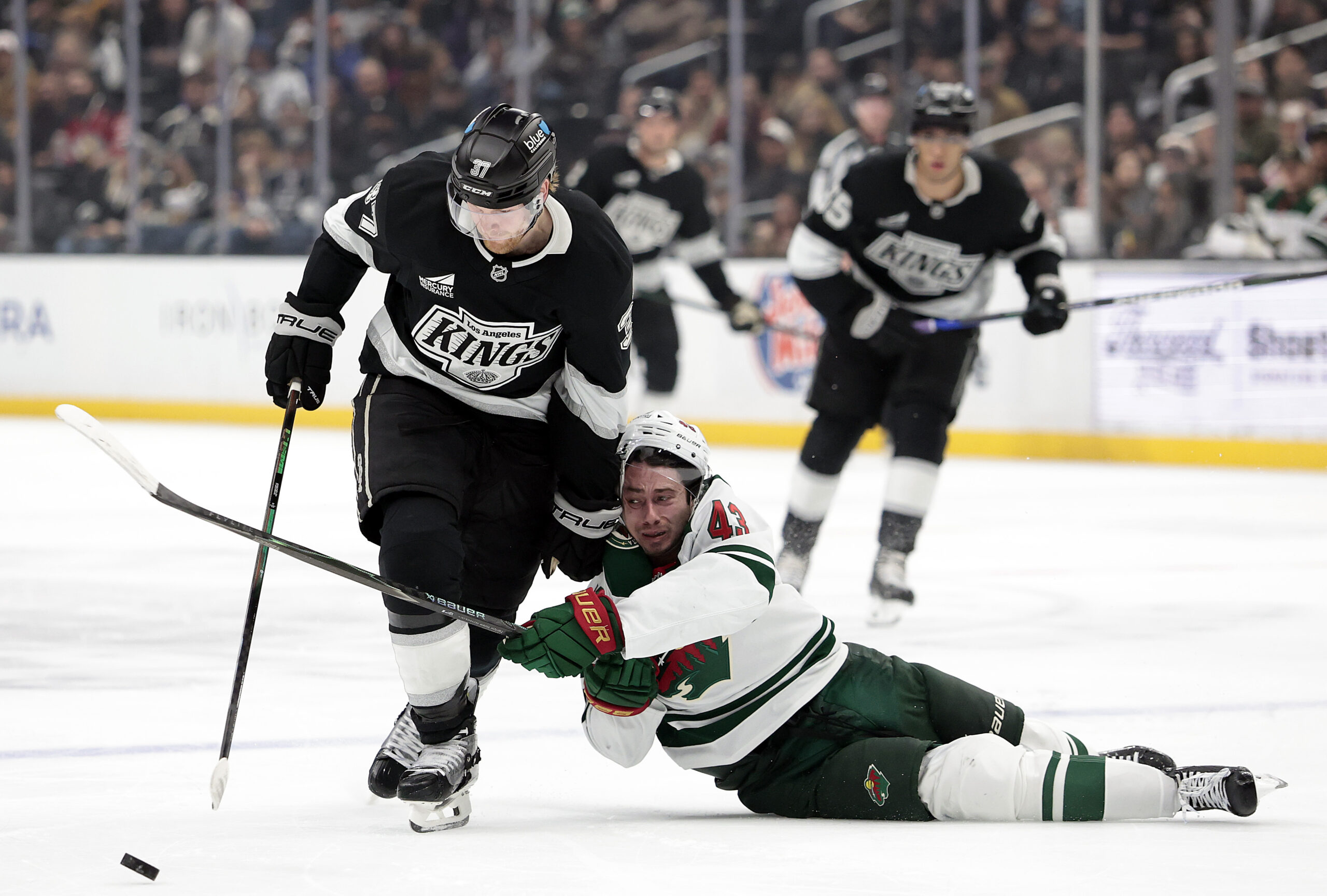 The Kings’ Warren Foegele, left, skates with the puck as...